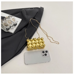 Close-up of golden acrylic mini evening bag with pearl-like embossed texture and chain