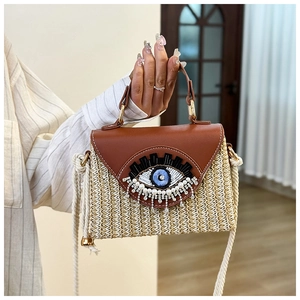 Détail d'un sac bandoulière en paille avec rabat en cuir et motif œil protecteur