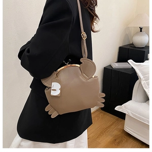 Detail of khaki crab-shaped crossbody bag with gold clasp and adjustable shoulder strap