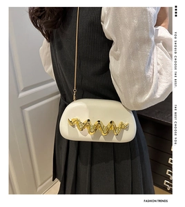 Detailed view of the wavy gold metal ornament on white leather evening clutch bag