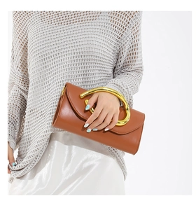 Detail of caramel leather clutch bag with golden circular metal handle on white outfit