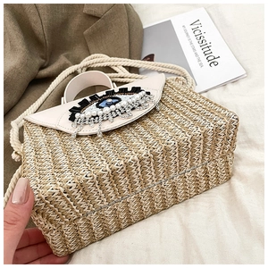 Détail d'un sac boîte en paille tissée avec motif œil perlé et bandoulière en coton