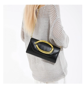 Detail of black envelope clutch featuring a gold oval buckle and elegant chain strap