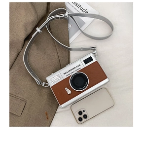 Detail view of silver and brown camera-shaped crossbody bag with adjustable strap and phone