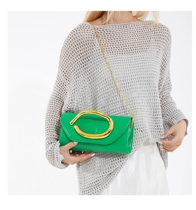 Detail of vibrant green leather clutch featuring a large gold oval metal handle and chain