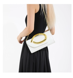 White envelope clutch with large oval gold handle and chain strap on a black dress model