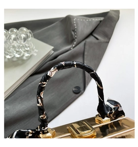 Detail of gold metallic handbag handle wrapped in black and white geometric silk scarf