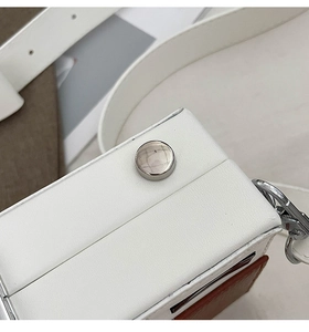 Close-up of stylish white camera bag featuring brown patchwork and silver metal stud detail