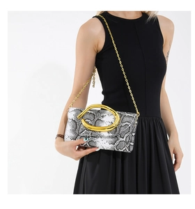 Detail of snake pattern clutch bag with gold oval clasp held by a model in a black dress