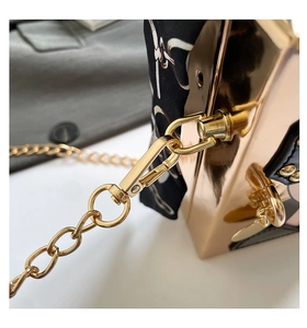 Detail of rose gold mirror metal clutch bag with silk scarf and gold chain hook