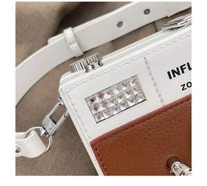 Detail of camera-shaped crossbody bag with silver knobs and white leather shoulder strap