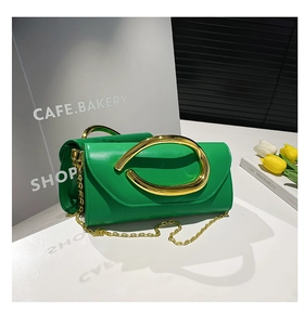 Detail of green glossy leather clutch with large gold metal ring handle and chain strap