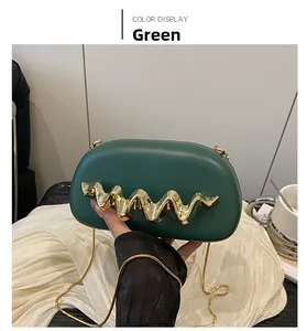 Detail of a dark green leather clutch bag with elegant wavy gold hardware and a chain strap