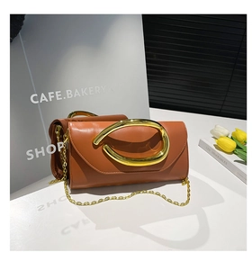 Detail of caramel leather clutch with sculptural gold ring buckle and elegant chain strap