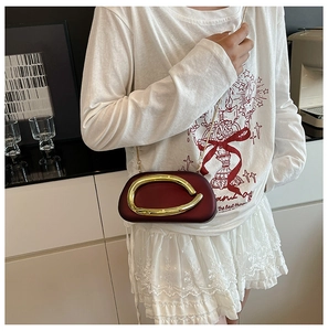 Detail of burgundy acrylic clutch bag with golden circular metal handle and chain strap