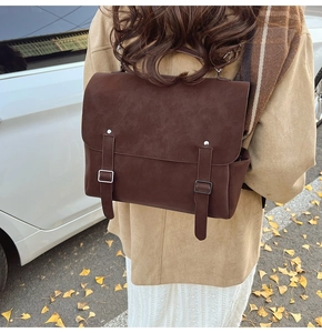 Detail of dark brown matte backpack with leather straps against an autumn street background