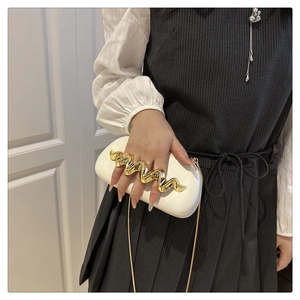 Detailed view of white acrylic clutch featuring gold wave handle and chain strap
