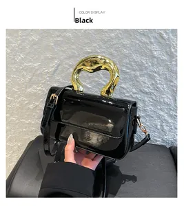 Detail of black glossy handbag featuring a unique chunky gold twisted handle and metal clasp
