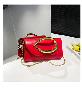 Detail of red clutch bag featuring unique large gold circular handle and thin metal chain