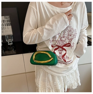 Detail of a dark green structured bag with a prominent gold circular buckle and chain strap