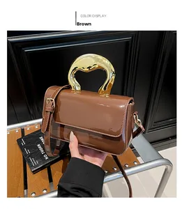 Detail of glossy brown handbag featuring a unique gold organic-shaped metal handle