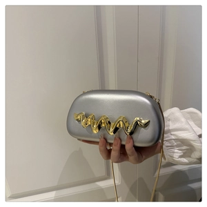 Detail of silver oval hard-shell clutch bag with golden wavy metal accessory and chain strap