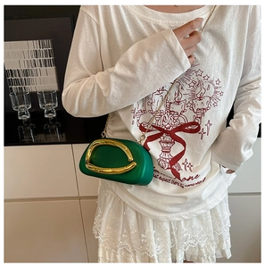 Detail view of grass green clutch bag featuring a prominent gold curved metal ornament
