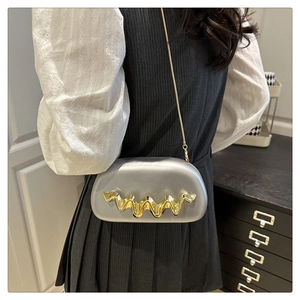 Detail of silver acrylic evening bag featuring gold wavy metal trim and slim chain strap