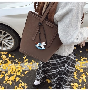 Detail of dark brown tote bag with horse charm on a model in autumn street setting
