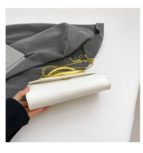 Detail view of white leather clutch bag with golden U-shaped handle and metal chain