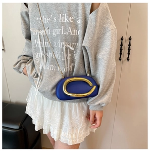 Detail of blue matte crossbody bag with gold C-shaped handle and fine metal chain