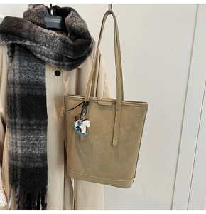 Detail of beige tote bag with a blue and white horse charm on a trench coat model