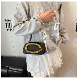 Detail of matte black oval crossbody bag with artistic gold handle and slim chain strap