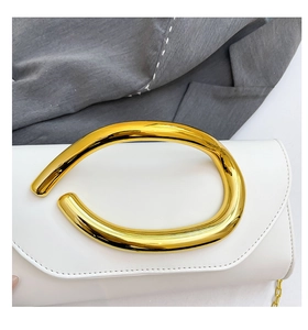 Detail of white leather clutch featuring a large golden abstract metal ring handle and chain