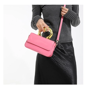 Detailed view of pink patent leather handbag with a large gold metal handle and strap