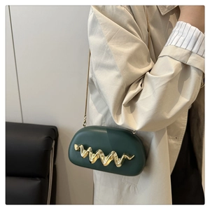 Detail of dark green acrylic evening bag featuring wavy gold hardware and a metal chain