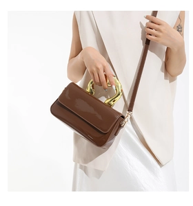 Detail of brown patent leather handbag with artistic irregular gold metal handle