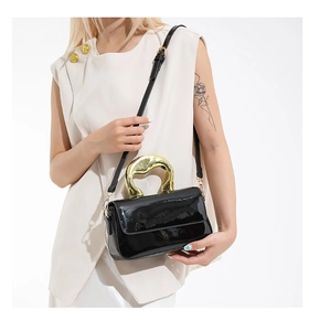 Detail of glossy black patent leather handbag featuring an artistic gold irregular handle