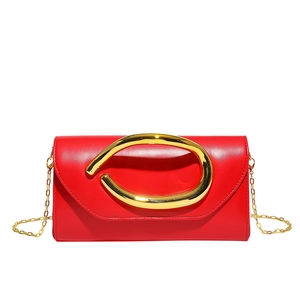 Detail of red leather envelope clutch featuring a large twisted gold metal handle