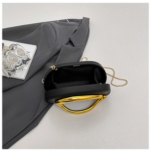Close-up of black luxury evening bag showing gold circular handle and fabric lining interior
