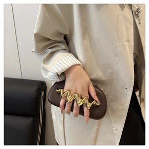 Macro shot of dark brown leather clutch featuring golden wave-shaped ring handle and chain