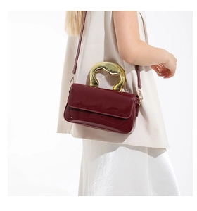 Detail of dark red patent leather shoulder bag with sculptural gold metal handle
