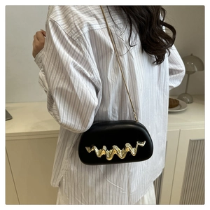 Detail of a chic black acrylic clutch with golden wave pattern and slim metal chain