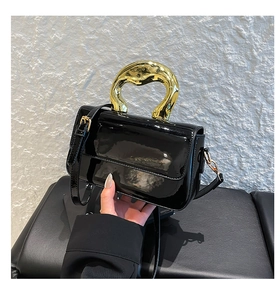 Detail of a black patent leather shoulder bag featuring a unique gold sculptural handle