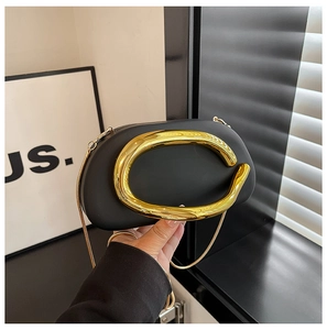 Detail of evening bag featuring a large gold C-shaped metal handle and chain strap