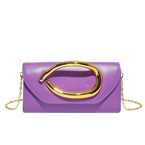 Detail of purple leather clutch with a large sculptural gold horseshoe handle and chain