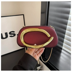 Detail of luxury burgundy evening bag featuring a large gold round metal buckle and chain