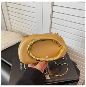 Macro detail of luxury cream evening bag featuring bold gold C-handle and snake chain