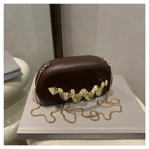 Detail of a dark brown acrylic evening bag with gold wavy metal trim and snake chain