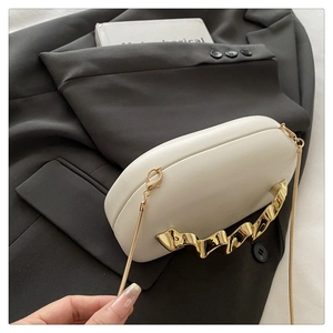 Detail of white leather clutch with unique gold wave handle and metal chain strap
